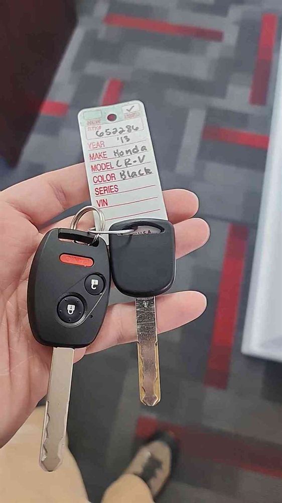 Two Honda keys held in hand next to a dealer tag for a 2013 Honda CR-V